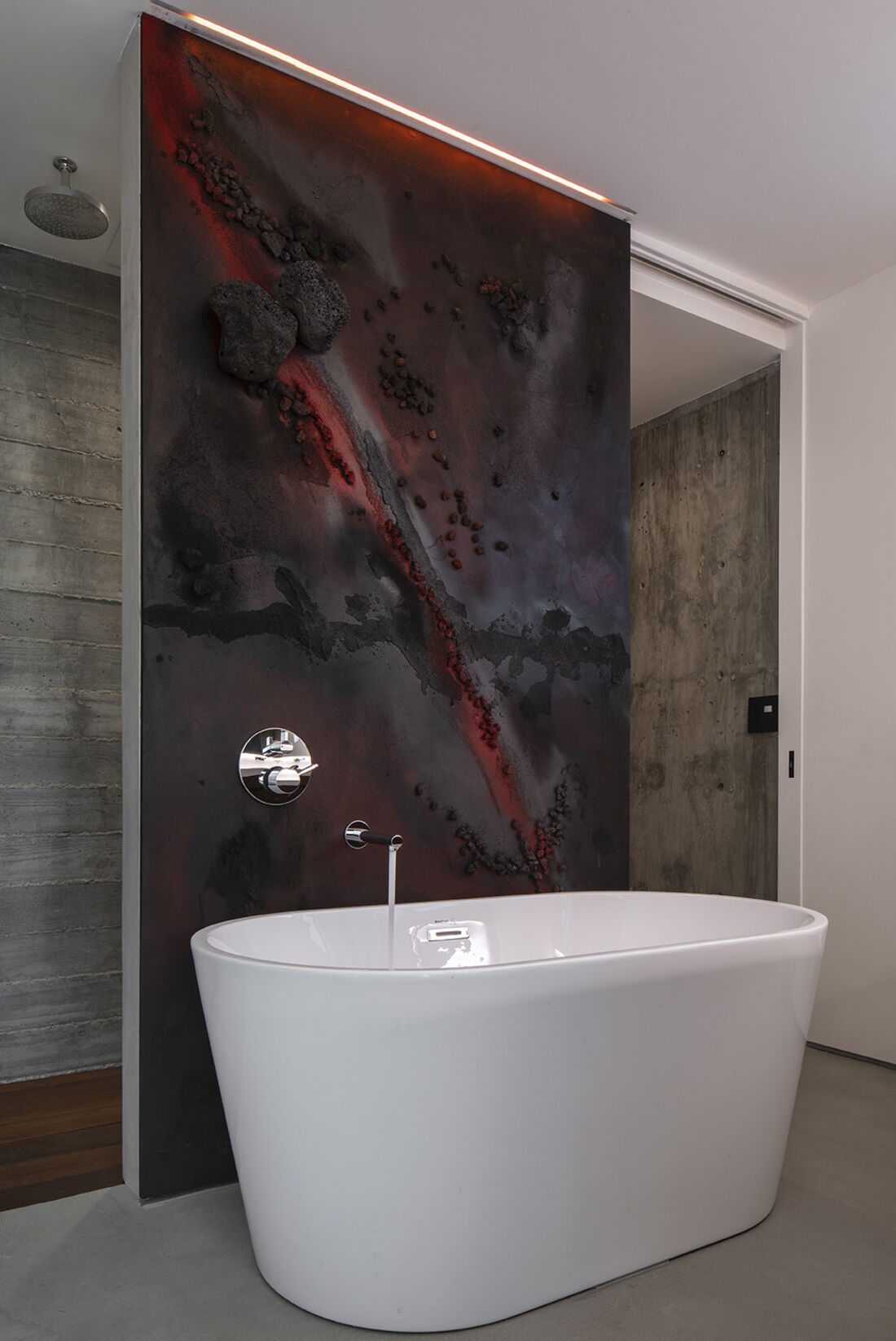 A black sand and obsidian wall behind a freestanding bathtub, grazed by a line of light