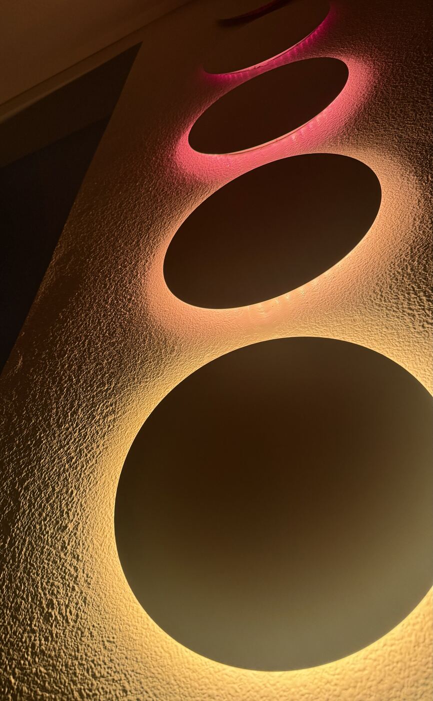 Close view of the Pentaclipse discs on a textured wall, glowing pink, amber and pale yellow