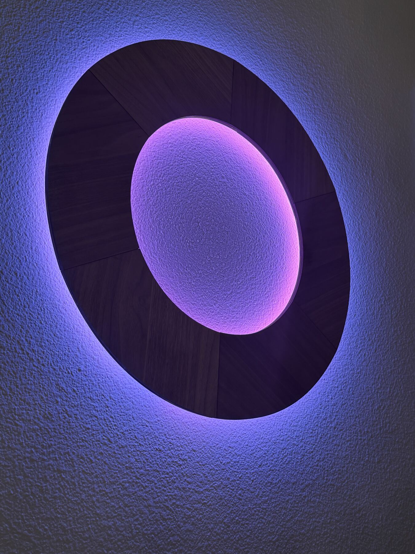 Chromaclipse O glowing violet with a pale lavender center against a light wall